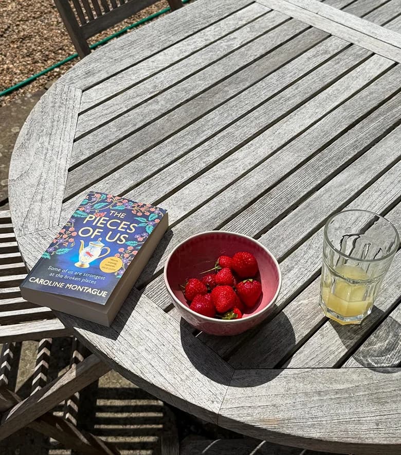 The Pieces of Us by Caroline Montague on an outdoor table with strawberries