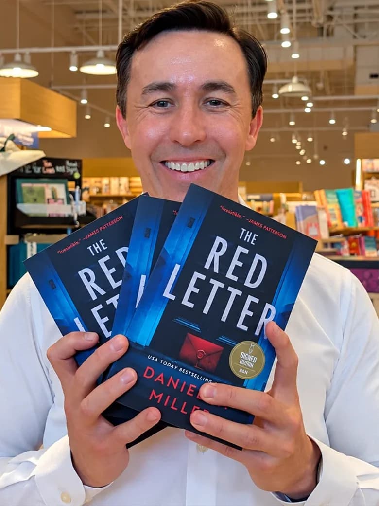 Daniel G. Miller smiling and holding multiple copies of The Red Letter in a bookstore